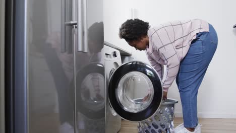 african american woman putting clothes into washing machine, doing laundry at home, slow motion