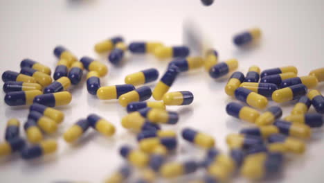 Macro-of-Blue-and-Yellow-Pills-Dropped-onto-White-Background