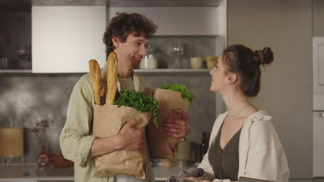 young couple shares an affectionate kiss after grocery shopping in their kitchen