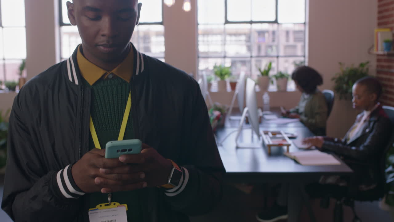 close up young african american man student using smartphone browsing social media messages texting on mobile phone walking in diverse office workplace