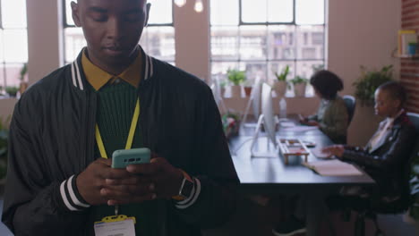 Cerrar-A-Un-Joven-Estudiante-Afroamericano-Usando-Un-Teléfono-Inteligente-Navegando-Mensajes-De-Redes-Sociales-Enviando-Mensajes-De-Texto-Por-Teléfono-Móvil-Caminando-En-Diversos-Lugares-De-Trabajo-De-Oficina