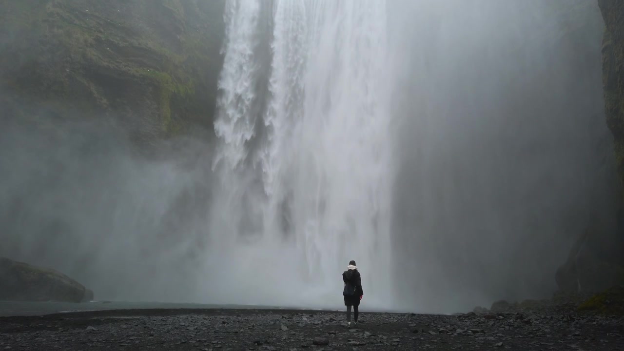 Exploradora solitaria haciendo senderismo cerca de la majestuosa y dramática cascada Skogafoss. Naturaleza islandesa inmersiva y destino de viaje.