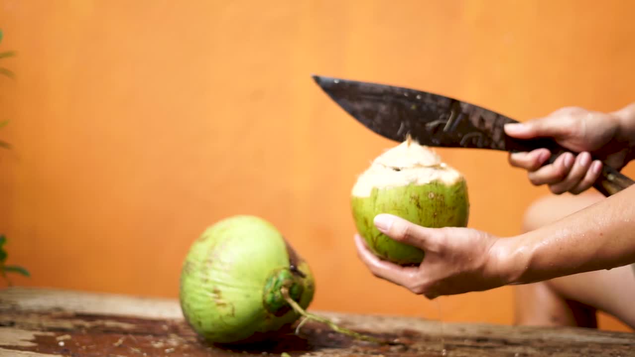 Video of woman cutting open a green coconut in Hawaii. With a machete and practiced hands, she prepares the tropical fruit—an authentic island moment of skill, refreshment, and tradition