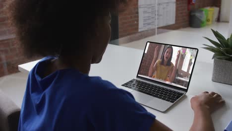 Back-view-of-african-american-woman-having-a-video-call-on-laptop-with-female-colleague-at-office