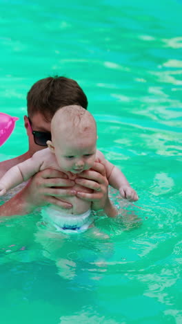 Happy family having a day off in the pool. Caucasian parents are resting in water with their baby on hot summer day.. Vertical video