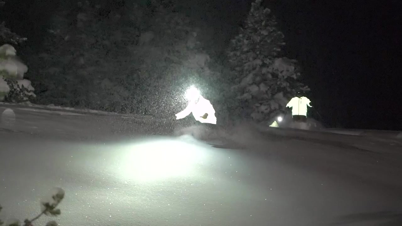 Kontrast mellem lys og mørke ved offpiste skiløb/snowboarding om vinteren om natten i snestorm ved Vail Pass, USA. Unikke pandelamper og fluorescerende jakke lyser