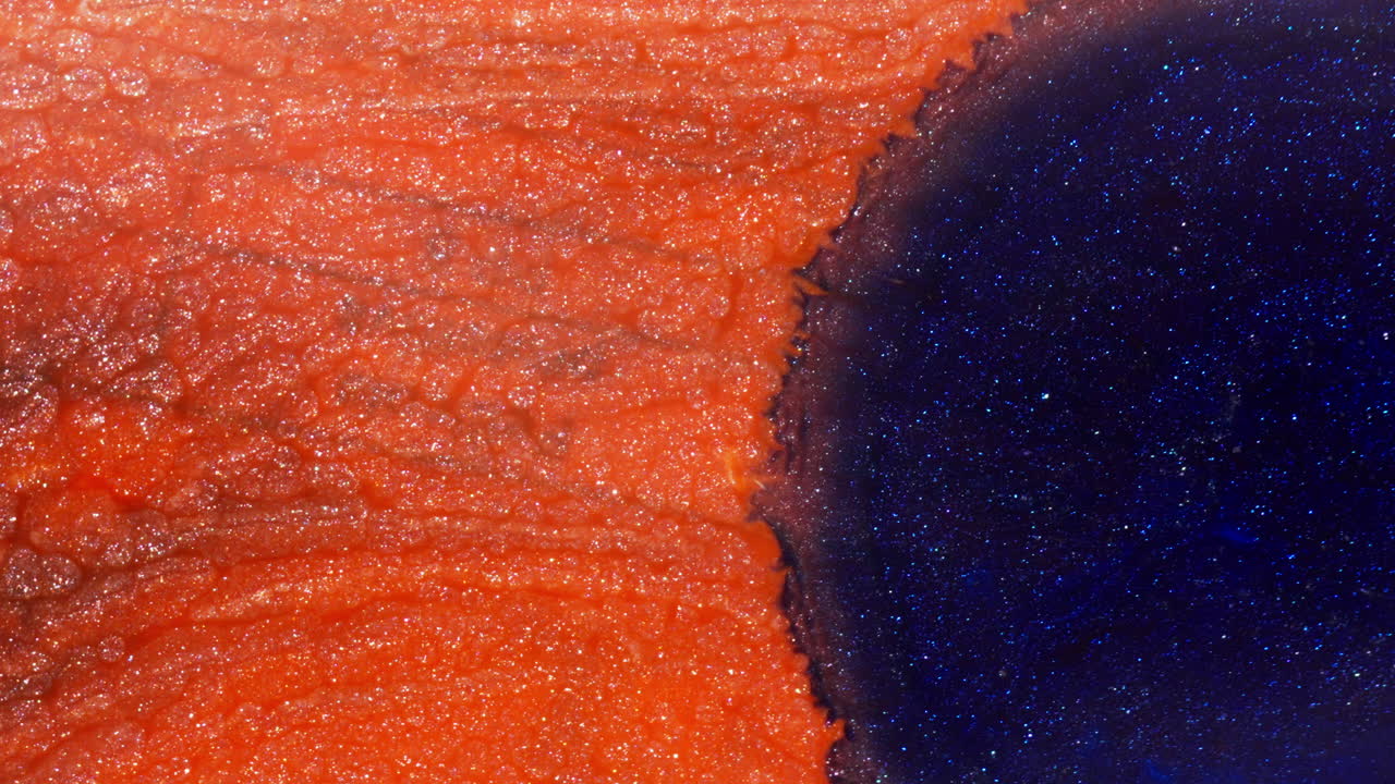 Dropping Blue Ink Onto Glittery Orange Ink, Forming Contrast Of Color And Texture. abstract