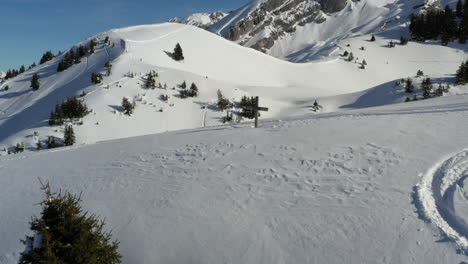 Aerial-view-flying-over-a-snowy-hill-top-with-a-wooden-cross-on-top,-in-the-French-Alps-in-winter