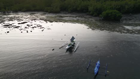 drone establishing orbit capturing the tranquil waters of taloot argao port at sunrise, with traditional boats anchored in shallow waters in cebu, philippines