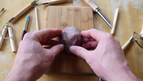 a sculptor shaping and forming a face out of brown modeling clay in an art studio with tools on the table