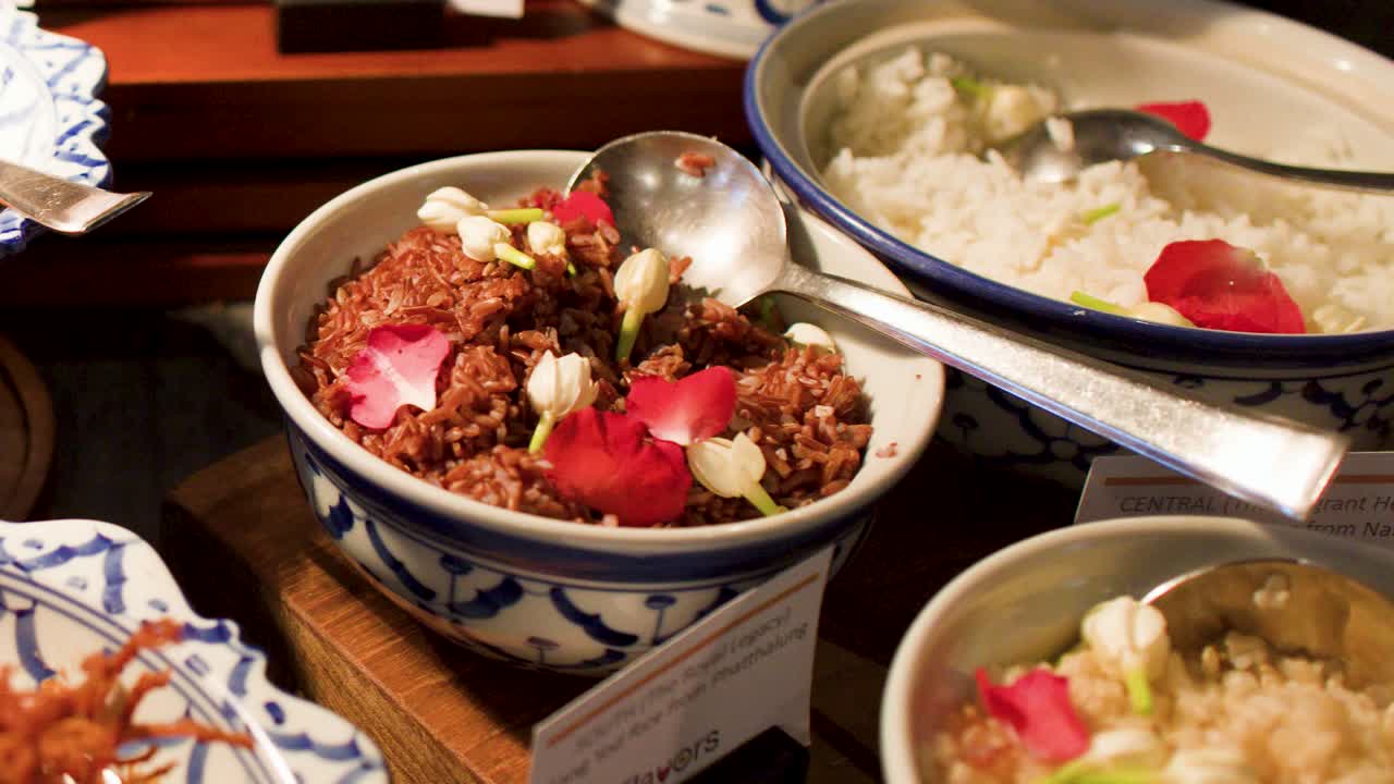 クローズアップカメラが、陶器の器に入った様々なタイの米料理と伝統的なスナックをパンする。