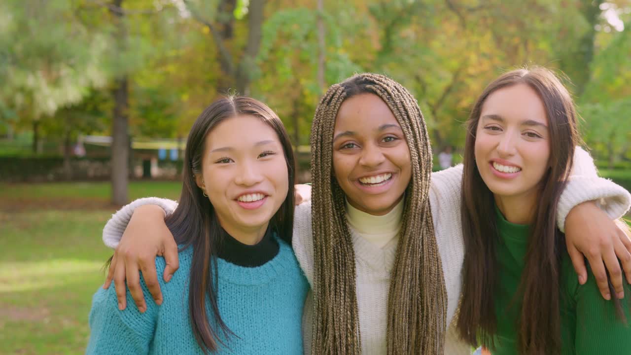 Three diverse young women smiling and embracing outdoors