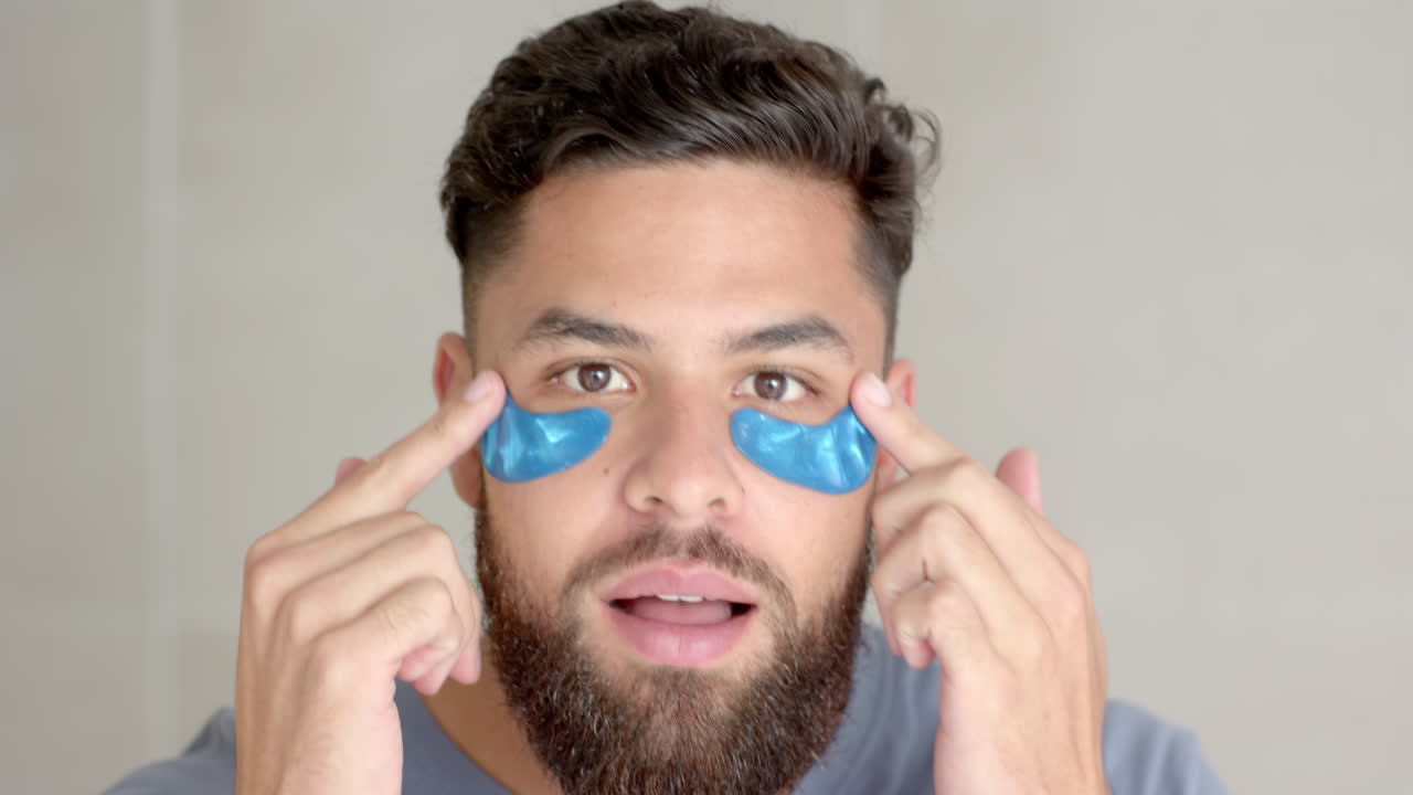 Applying under-eye patches, man focusing on skincare routine at home