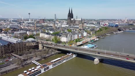 aerial dolly out of cologne city center skyline and cathedral over cruise ship dock and rush hour traffic on deutzer bridge