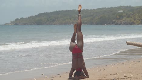 un contorsionista en una posición de pie de mano antes de desmontar en una pose con olas rompiendo la costa en el fondo