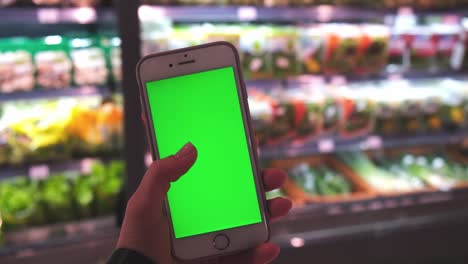 chroma key. close up of woman holds smart phone with green screen at grocery store. shopping center. department store. mall. shopping online