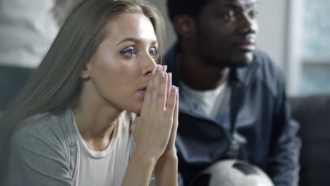 closeup of young beautiful woman watching soccer game on tv and covering face with hands while getting sad about team failure