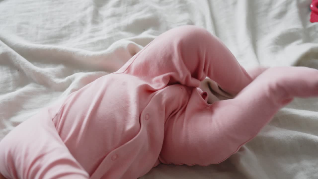 adorable bebé pateando mientras está acostado en la cama con traje rosa, vista de arriba hacia abajo