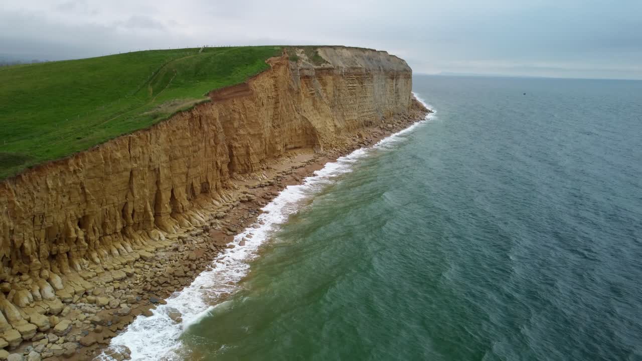 Aerial footage over the cliffs of the Jurassic Coast, Dorset. The footage starts panned down over the deep blue sea, then move backwards and pans up to reveal the cliff faces in their full glory.