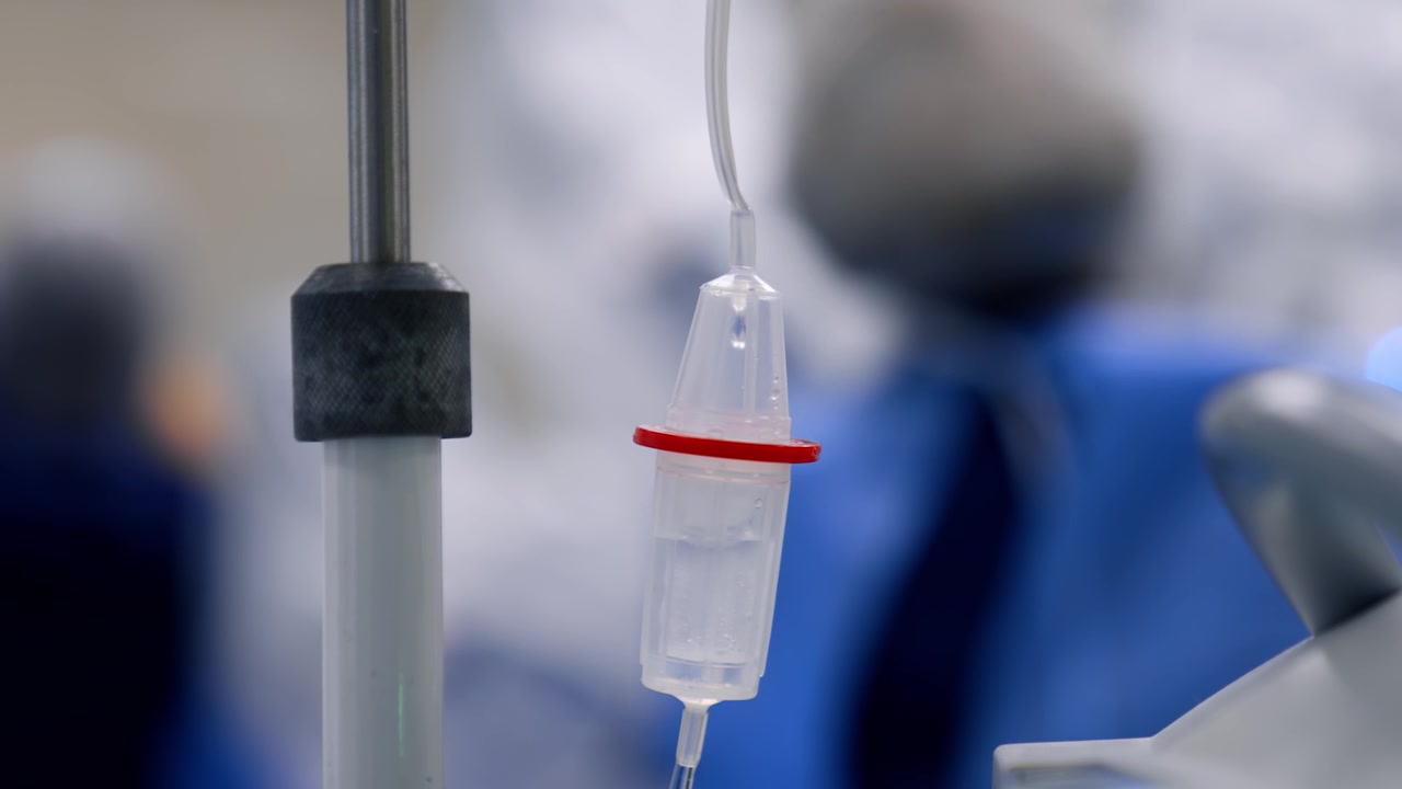 Soluzione fisiologica che gocciola rapidamente all'interno del deflussore. Primo piano. Medici sullo sfondo, sfocati.