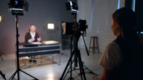 young woman with long brunette hair filming a lady sitting at desk. studio footage of a program.