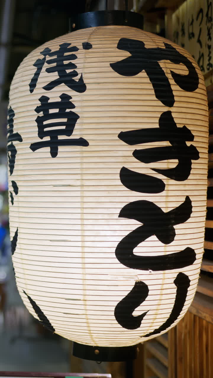 Tokyo, Japan - April 23, 2025: Close up of a white paper lantern on the underground subway with people walking by in the blurred background. Vertical. Translation: "Yakitori Asakusa"