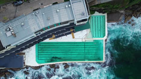 Un-Dron-Disparó-Sobre-La-Piscina-De-Iceberg-De-Bondi-Beach-Con-Olas-Rompiendo-En-La-Costa-En-Sídney,-Australia