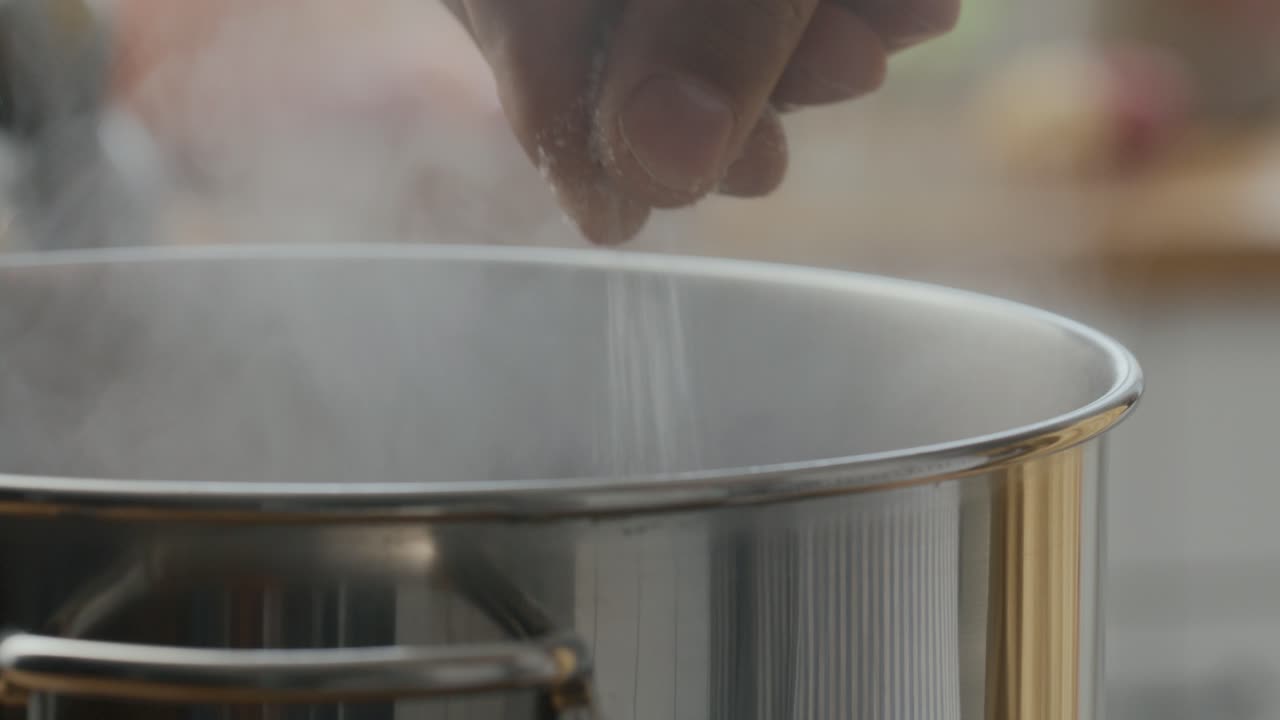 Hand Adding Salt into Steaming Pot during Cooking in the Kitchen