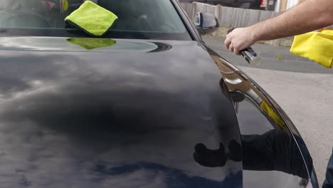 applying a spray sealant to a black car bonnet hood