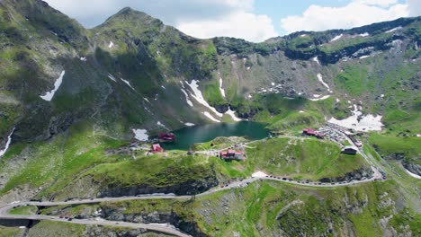 Aerial-View-Of-Balea-Lake-And-The-Famous-Transfagarasan-Mountain-Road-In-Romania,-Aerial-View-Of-A-Beautiful-Mountain-Range-With-High-Peaks,-Thick-Fluffy-Clouds-And-A-Beautiful-Green-Valley