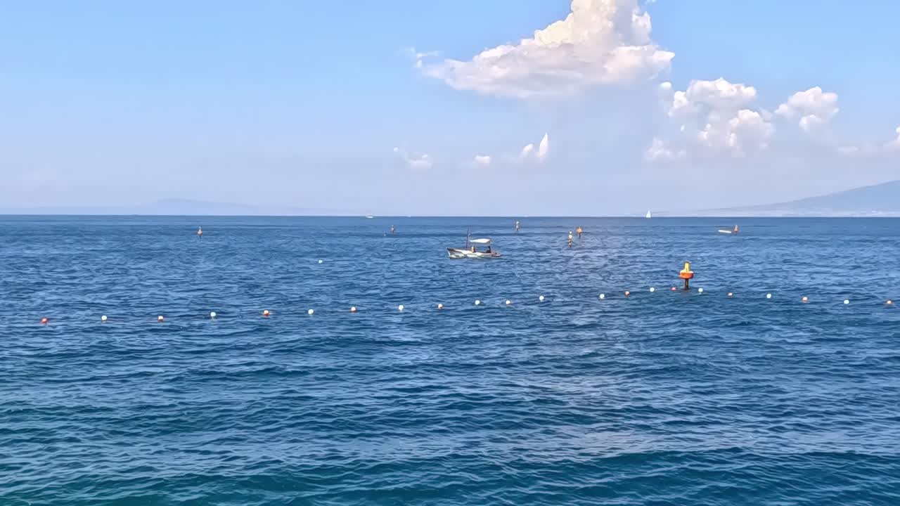 Calm ocean waters with scattered buoys and a distant mountain under a clear blue sky.