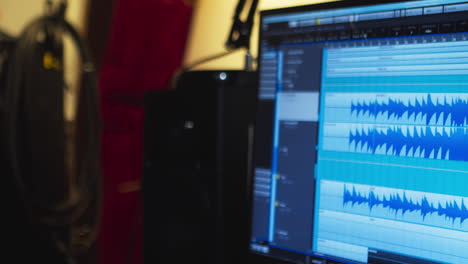 woman in a recording studio sits in front of a computer monitor displaying sound waves