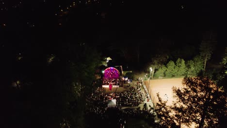 4k drone footage of live music concert, illuminated stage and the crowd in the park at nighttime