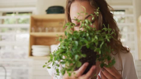 happy caucasian woman smelling plant standing in cottage kitchen