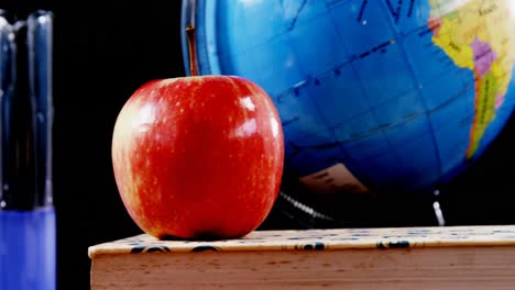 apple on book with globe against black background