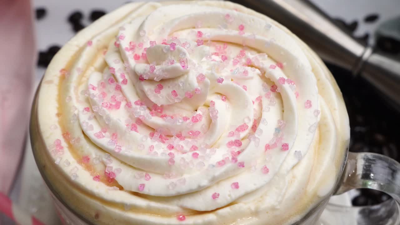 Dessert pink coffee in a mug topped with whipped cream and sugar sprinkles. Delicious and sweet dessert hot coffee in a coffee mug and surrounded by coffee beans.