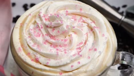 dessert pink coffee in a mug topped with whipped cream and sugar sprinkles. delicious and sweet dessert hot coffee in a coffee mug and surrounded by coffee beans.