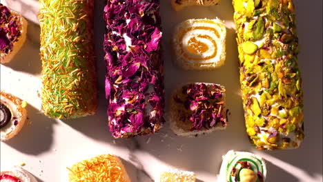 rotating camera movement captures a colorful assortment of turkish delight varieties, garnished with rose petals, kataifi, pistachios, and decorative swirls—elegantly arranged on a marble surface