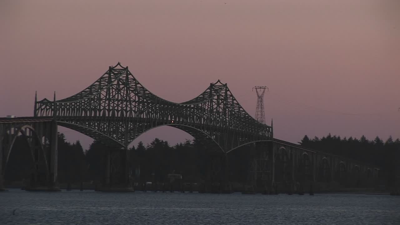 복잡하게 디자인된 금속 대들보로 보강된 우아한 다리를 타고 차량들이 강을 건너고 있습니다.
