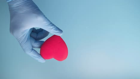hand in glove holding a pink heart