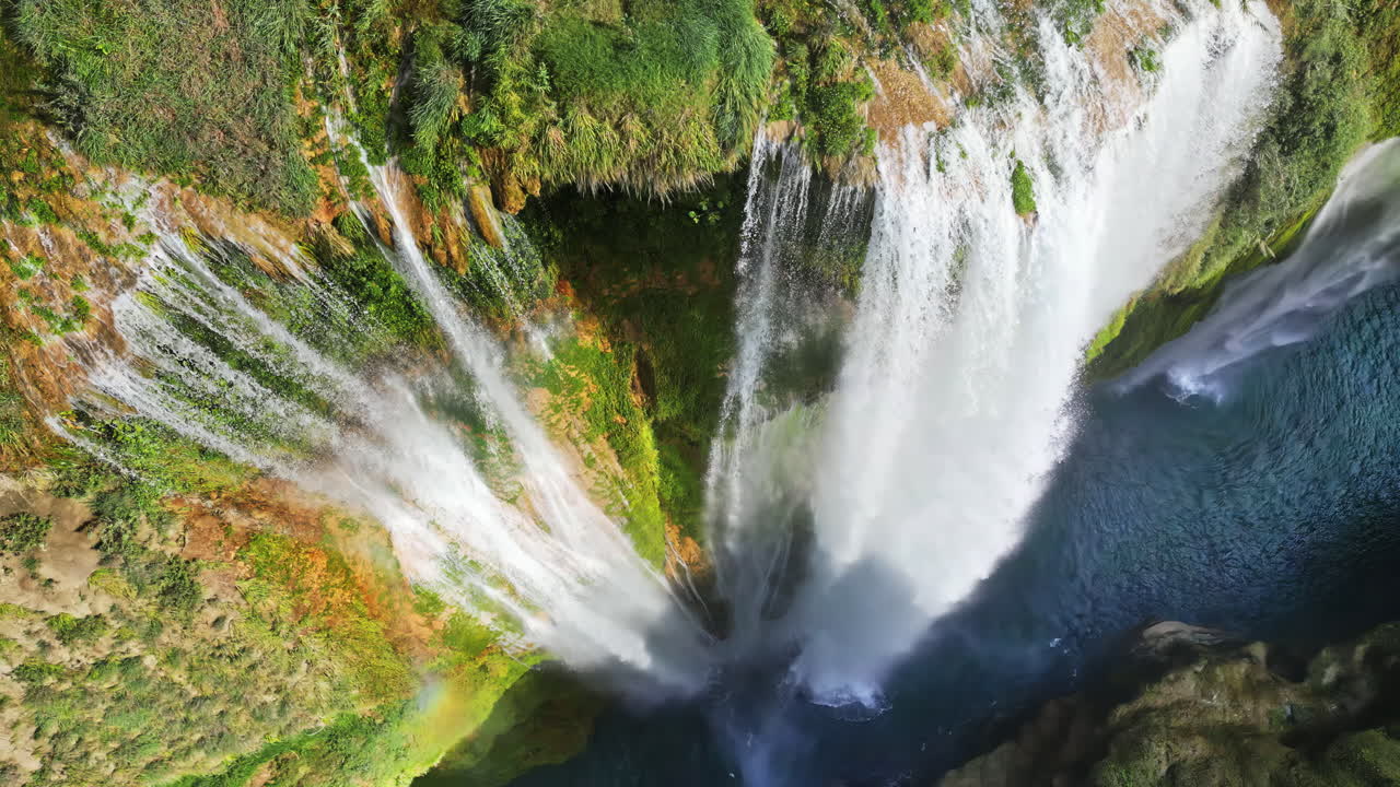 Aerial drone view of Tamul Waterfall cascading down green cliffs into a turquoise pool below in slow motion