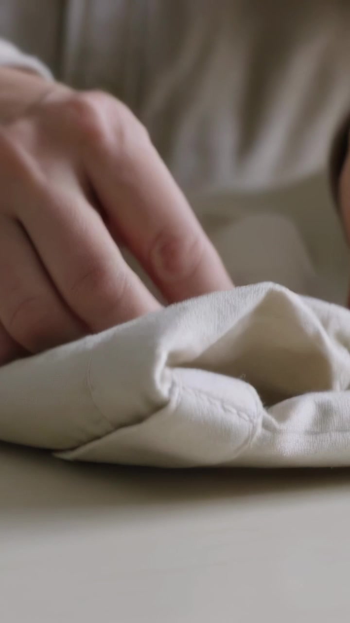 Vertical video: Entering hands smoothing beige shirt on table, making crisp cuff fold for storage