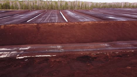 Peat-extraction-site-of-rural-area-on-snowy-winter-day,-aerial-side-view