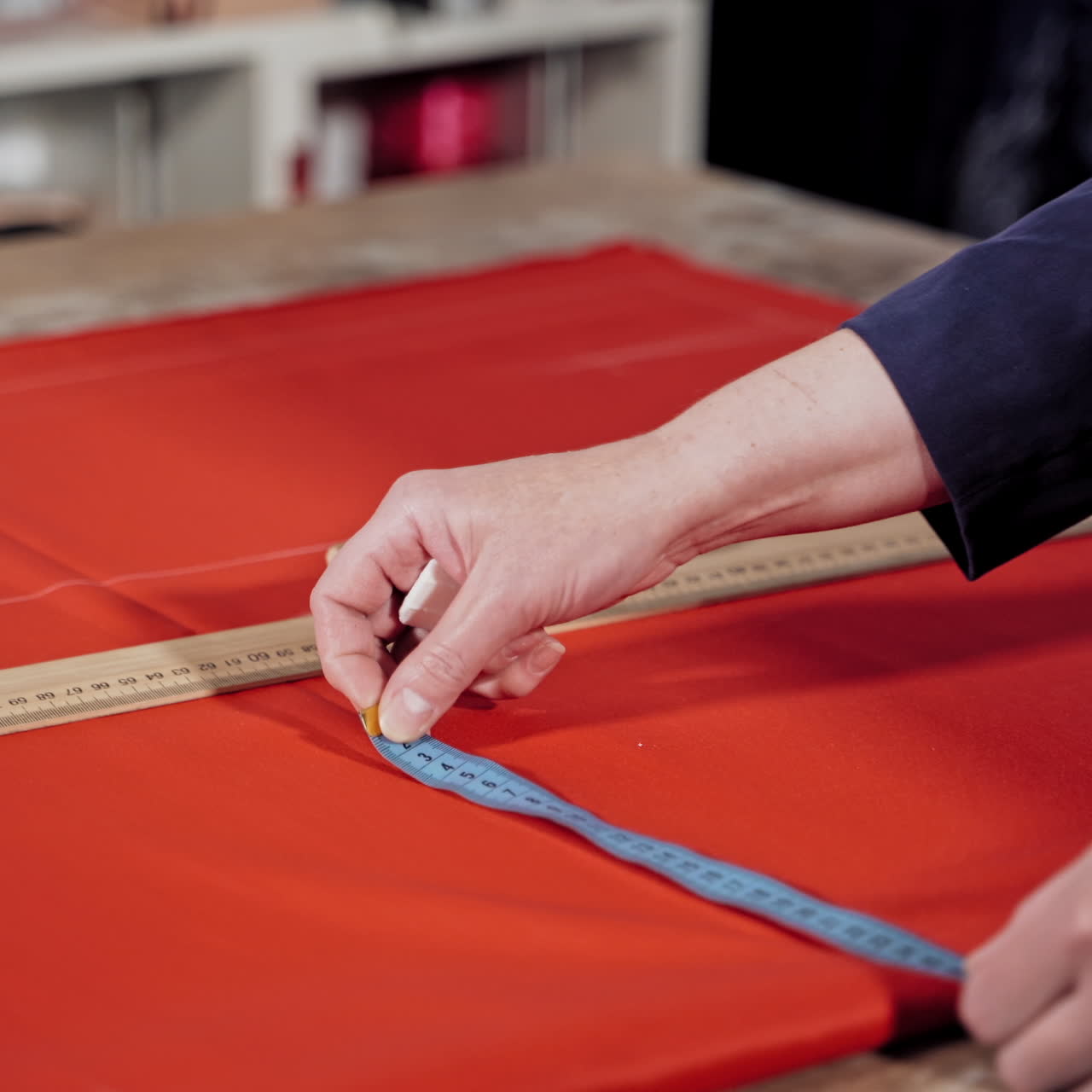 Female tailor is drawing sketch lines with a soap and a ruler on red fabric. Preparing details of material for new, modern dress or other clothes. Feminine hobby.