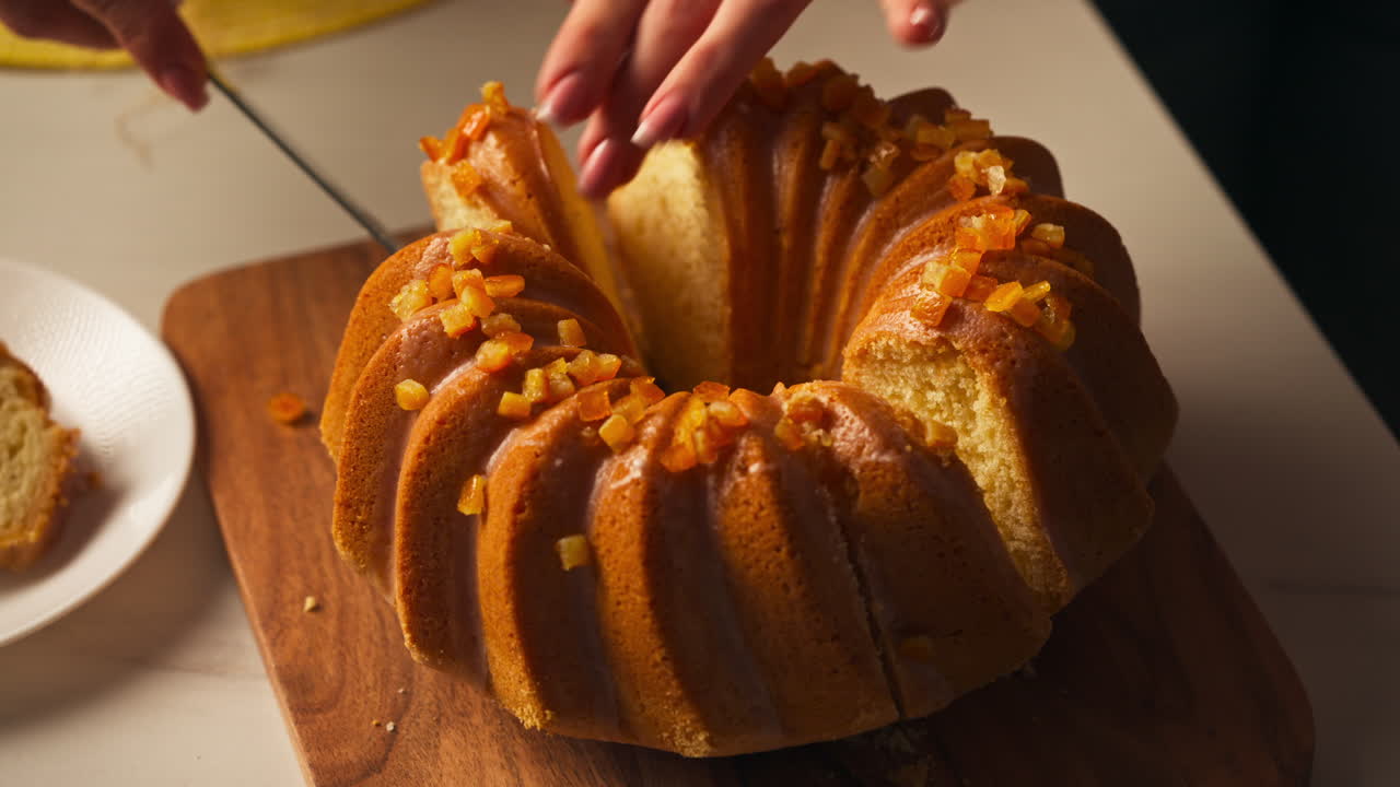 Şekerlenmiş portakal kabuklarıyla süslenmiş sırlı Bundt kek dilimleme - Paskalya Yemeği. Yakın çekim, yüksek açı çekim.