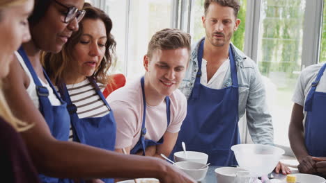 female student making flatbread on cooker in cookery class as adult students look on