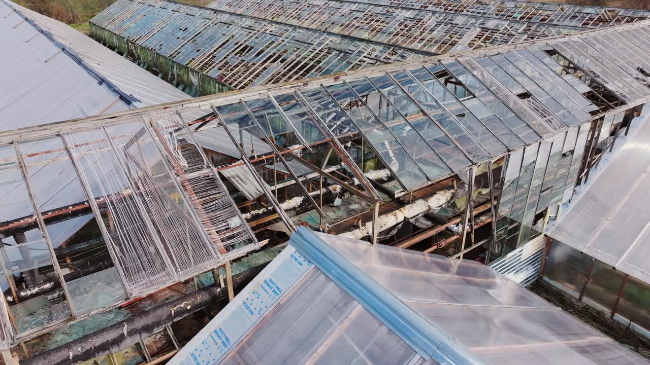 Abandoned glasshouse complex shows decay and neglect from a drifting aerial view