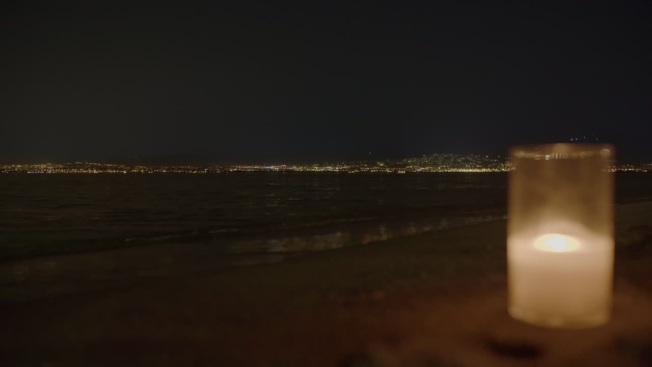 Flimrende stearinlys med fjerne bylys på stranden