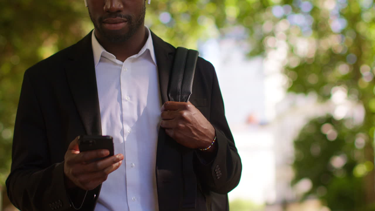 Young Businessman Wearing Wireless Earbuds Streaming Music Or Podcast From Mobile Phone Walking To Work In Offices In The Financial District Of The City Of London UK 4