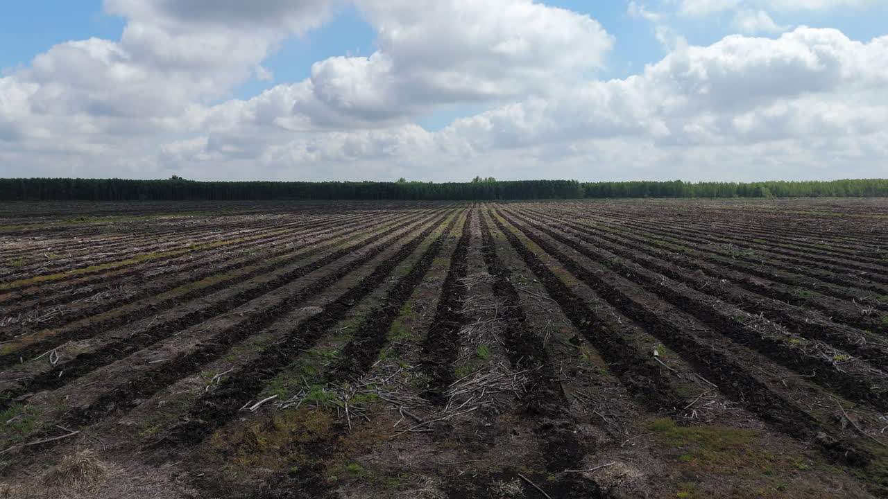 Aerial tracking right across tilled vast fertile farmland with dark soil, cultivated fields, and open skies